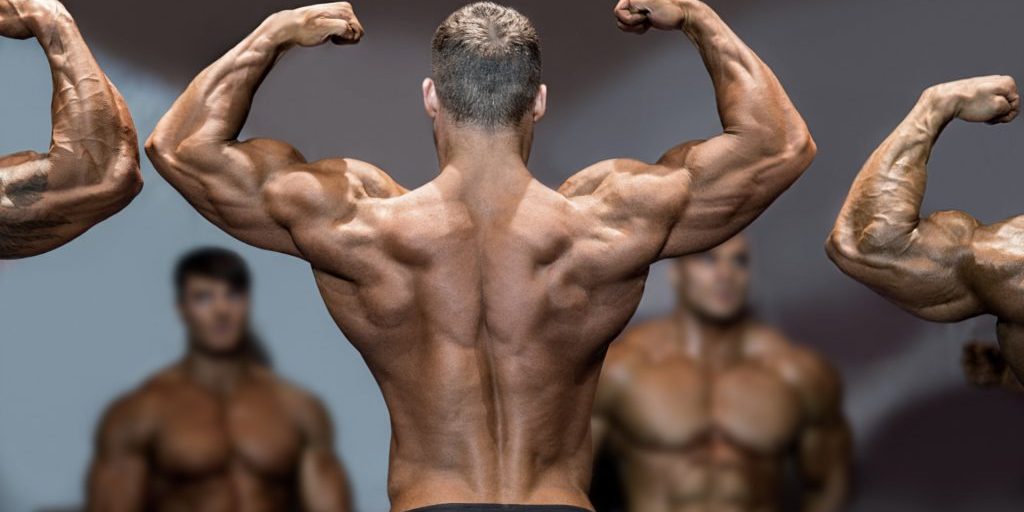 Bodybuilder flexing back and biceps. Muscular athlete posing on stage. Top sportsmen at bodybuilding competition. Opponents are watching.